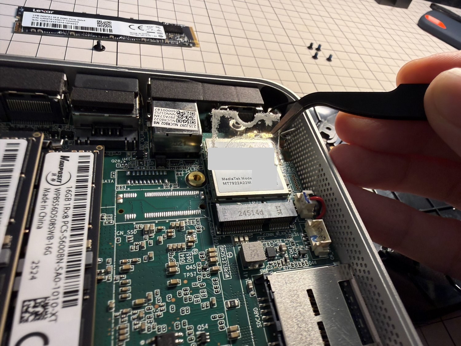GEEKOM A8の基板。Wi-Fiカードの上の透明なアクリル板をピンセットで外しているところ